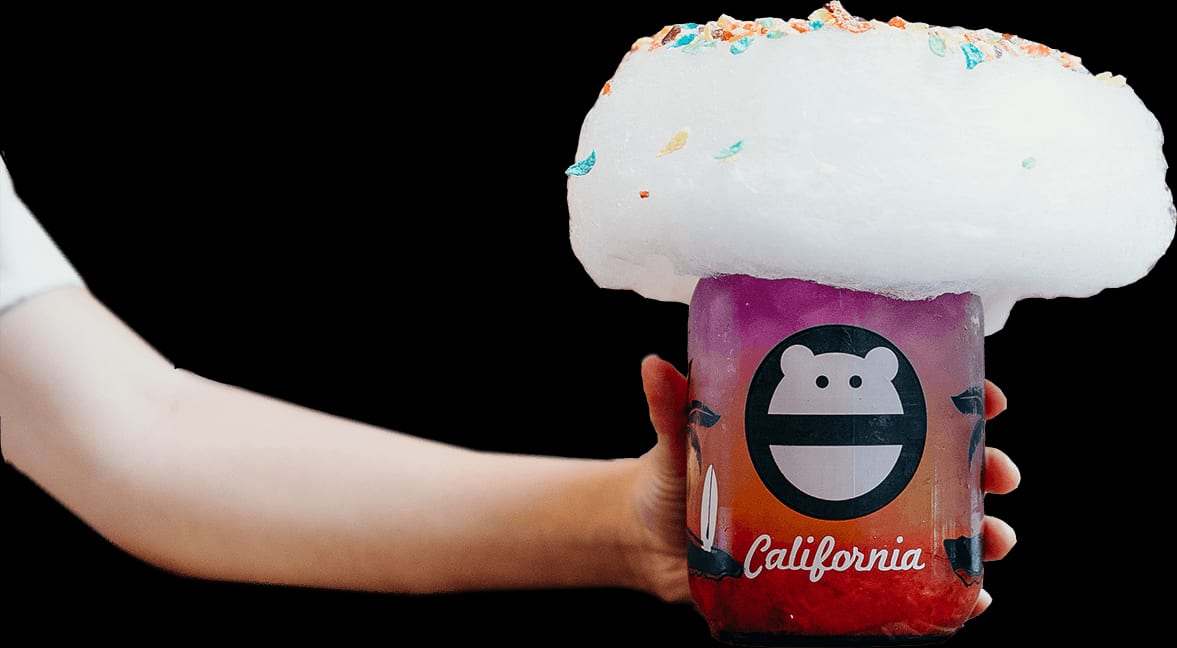 Outstretched arm holding a purple-to-red ombre drink in a monster-face “California” jar topped with a huge dome of cotton candy and rainbow cereal sprinkles